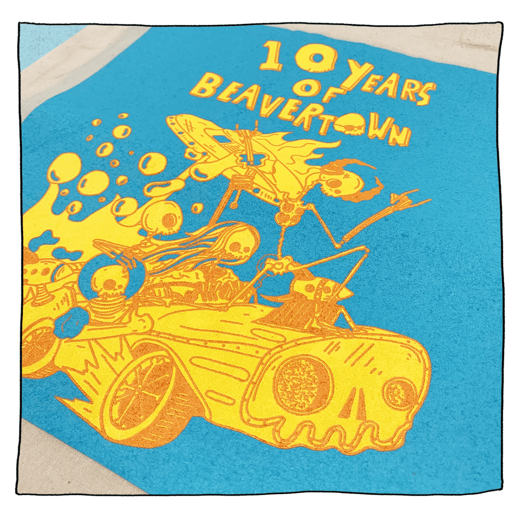 Beavertown Brewery 10th Birthday Tote Bag. Print on tote bag is blue and has a yellow and orange illustration of skeletons riding a car with a UFO behind them.