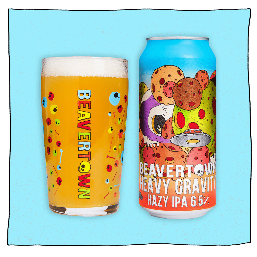 Heavy Gravity Hazy IPA and Psychedelic Pint glass filled with beer in front of a blue background. Can is blue with colourful meteors, a white skull and a silver UFO.