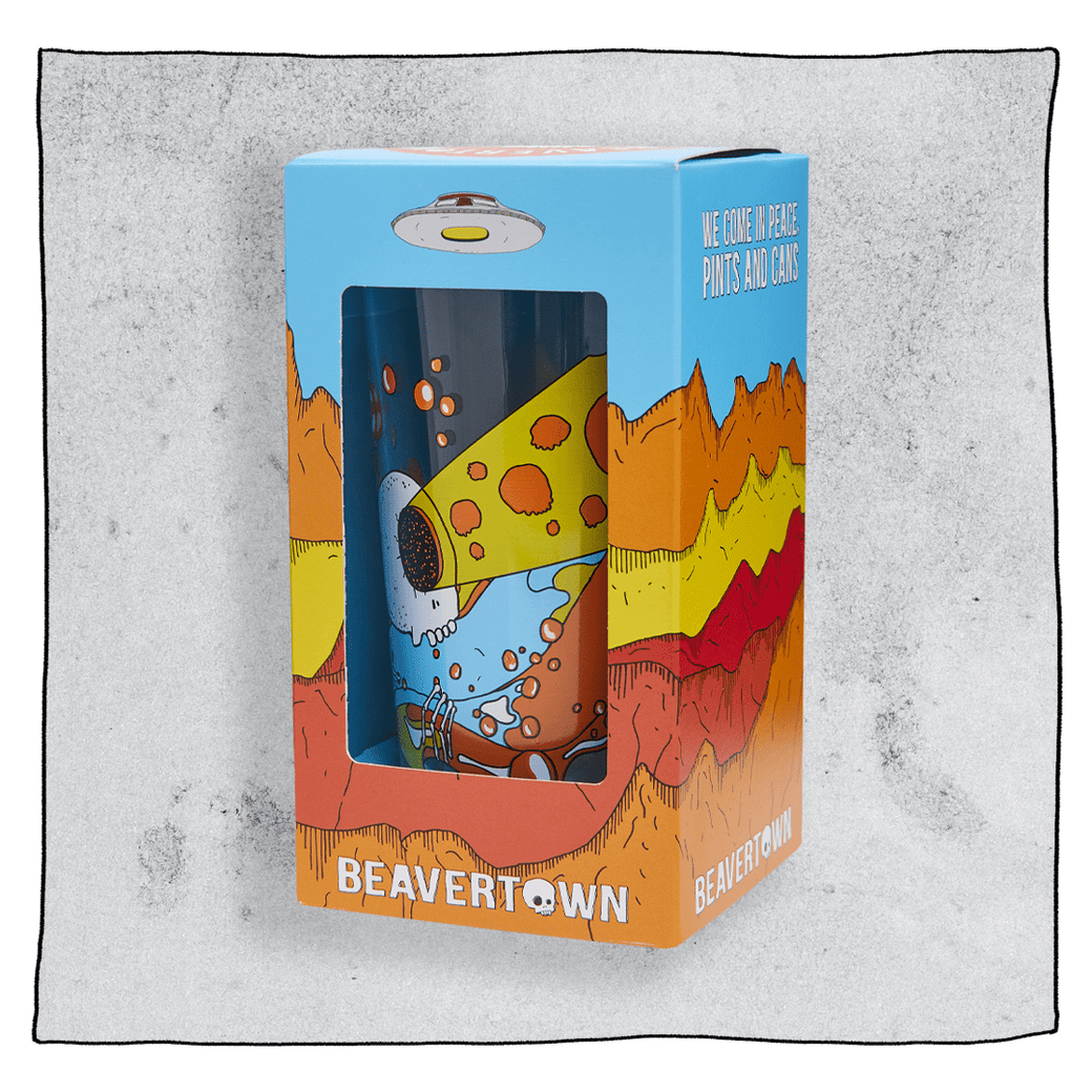 Beavertown Bones pint glass inside an orange and blue box in front of a grey background. Box has artwork depicting a white UFO in an orange, yellow and red canyon with a blue sky. Bones pint glass is visible in middle of box and is clear glass with logo of white skull with one eye socket shooting yellow beam amongst orange and blue streaks. Grey background.
