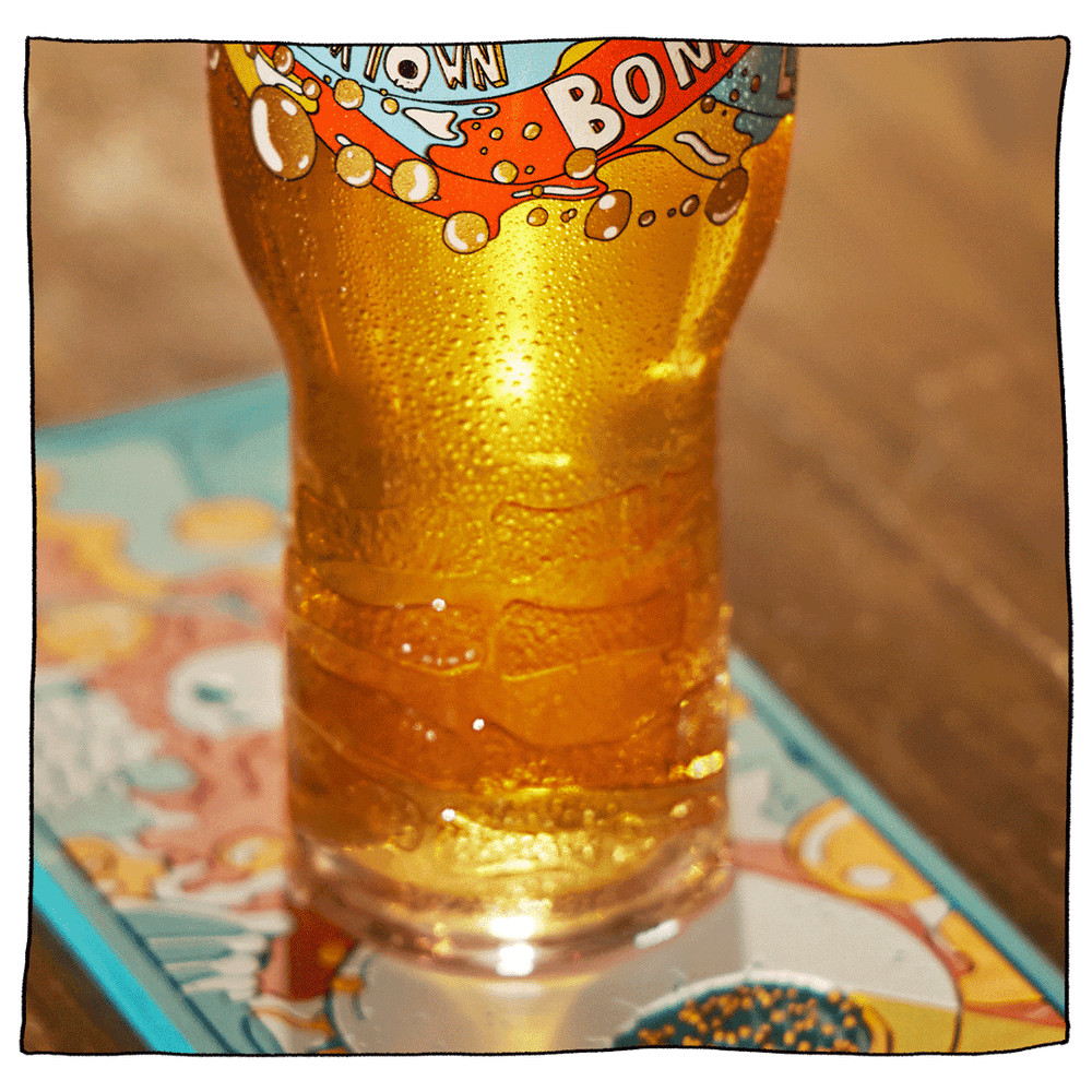 Beavertown Bones Skeletal Hand Pint Glass. Zoomed in on lower half of glass filled with beer and has a white Beavertown logo amongst orange and blue streaks. Image focused on the skeleton hand grooves engrained on lower half of glass. Glass sitting on Beavertown beer runner with brown bar background.