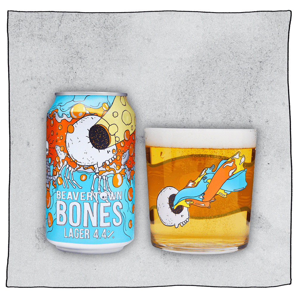 Beavertown Brewery Bones Lager Can and Beavertown Bones Tumbler glass filled with beer in front of a grey background. Beer glass is clear glass that has a white skull with one eye socket shooting yellow beam amongst orange and blue streaks.