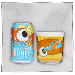Beavertown Brewery Bones Lager Can and Beavertown Bones Tumbler glass filled with beer in front of a grey background. Beer glass is clear glass that has a white skull with one eye socket shooting yellow beam amongst orange and blue streaks.