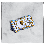 Bones Pin Badge. Left side angled view. White bones badge with orange and blue outline of text and white skull with orange eye instead the letter 'O'. Grey background.