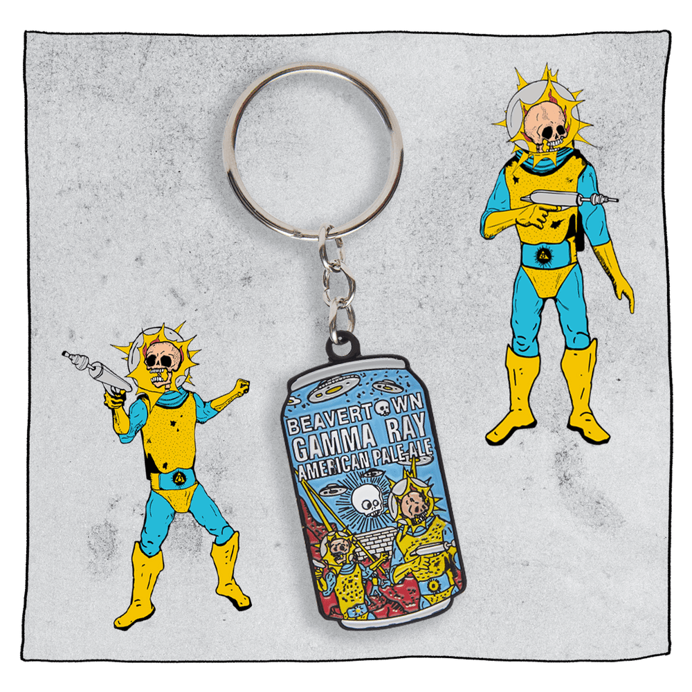 Gamma Ray Keyring with light grey background and 2 Gamma Astronauts next to the key ring. Key ring is a replica of the Gamma Ray can - blue, and orange with Gamma Astronauts in the foreground.