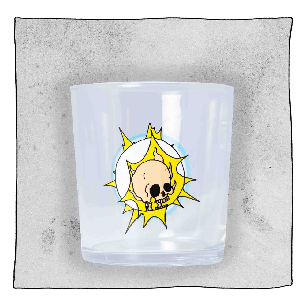 Beavertown Gamma Ray Tumbler glass in front of a light grey background. Beer glass is clear glass that has a salmon pink skull inside a white space helmet with yellow flashes.