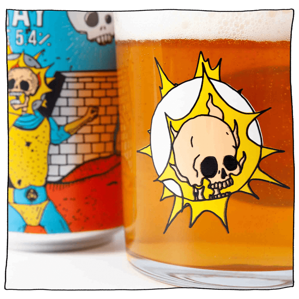 Zoomed in image of Beavertown Gamma Ray Tumbler Glass filled with beer next to a Gamma Ray American Pale Ale can. Tumbler Glass has skull inside a space helmet with yellow sparks around it.