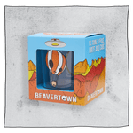 Beavertown Neck Oil tumbler glass inside an orange and blue box in front of a grey background. Box has artwork depicting a white UFO in an orange, yellow and red canyon with a blue sky. Neck Oil tumbler glass is visible in middle of box and is clear glass with an orange and white skull hot air balloon. Grey background.