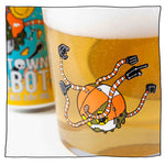 Zoomed in image of Nanobot Tumbler glass filled with beer with Nanobot can in the background. Nanobot logo is orange and white with black hands.