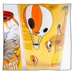 Zoomed in shot of Neck Oil pint glass filled with beer in front of a light grey background with a Neck Oil can next to it. Glass has many orange and white skull hot air balloons.
