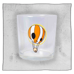 Empty Neck Oil Tumbler glass in front of a light grey background. Glass is clear with an orange and white skull hot air balloon.