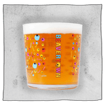 Psychedelic tumbler glass filled with beer in front of a grey background. Glass is clear with colourful skulls and bones scattered all around the glass.