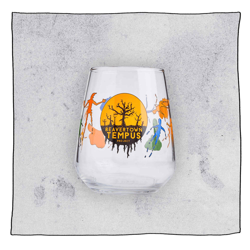 Empty Tempus Tumbler glass in front a grey background. Glass has orange and black dead tree Tempus logo.